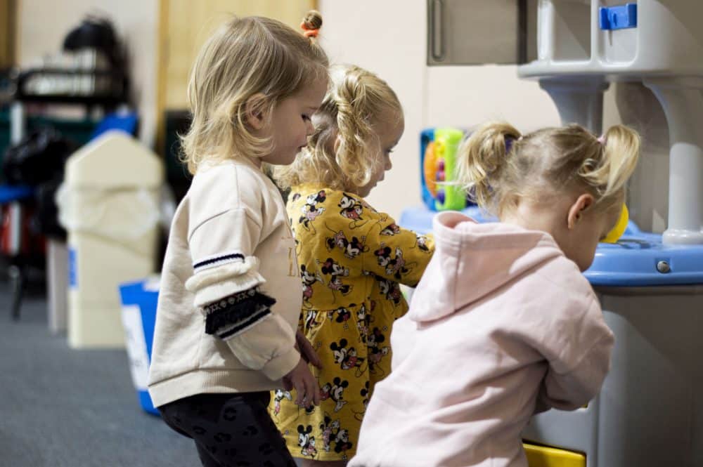 three children playing with a toy kitchen