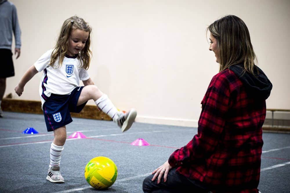 a child kicking ball to mum