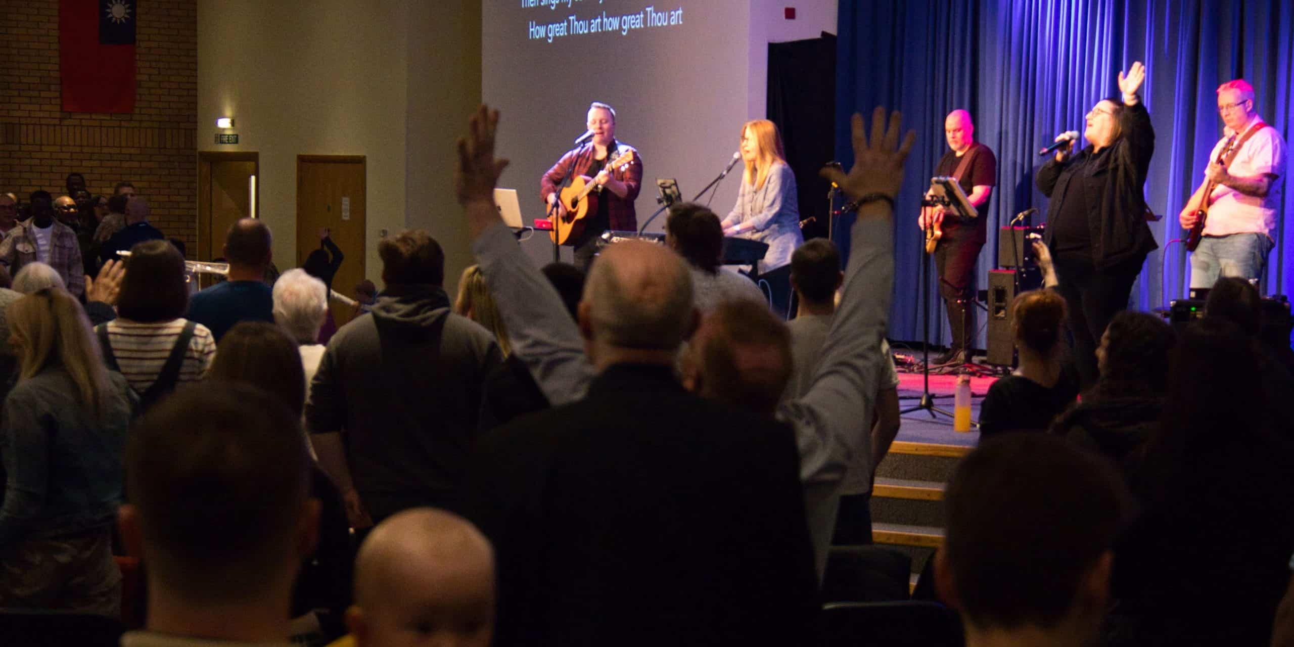 The congregation at TVCC worshipping, some with hands raised. The TVCC worship team is leading a song on the stage.