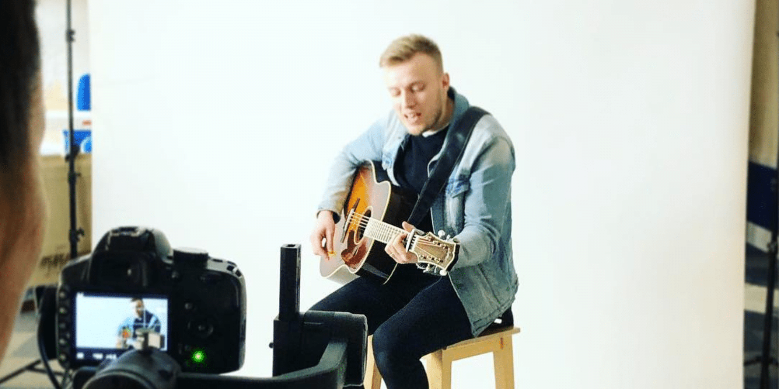 Will Horner playing the guitar and being recorded on a camera in the foreground
