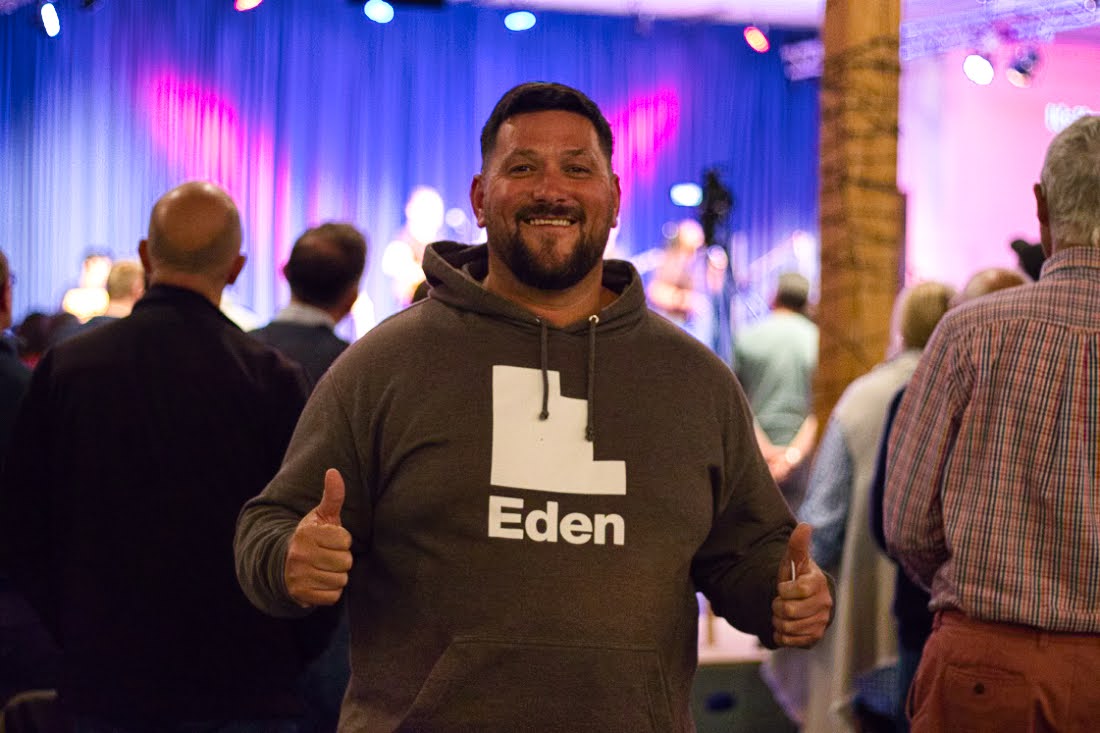 Man smiling at the camera with two thumbs up, wearing an Eden Team hoody