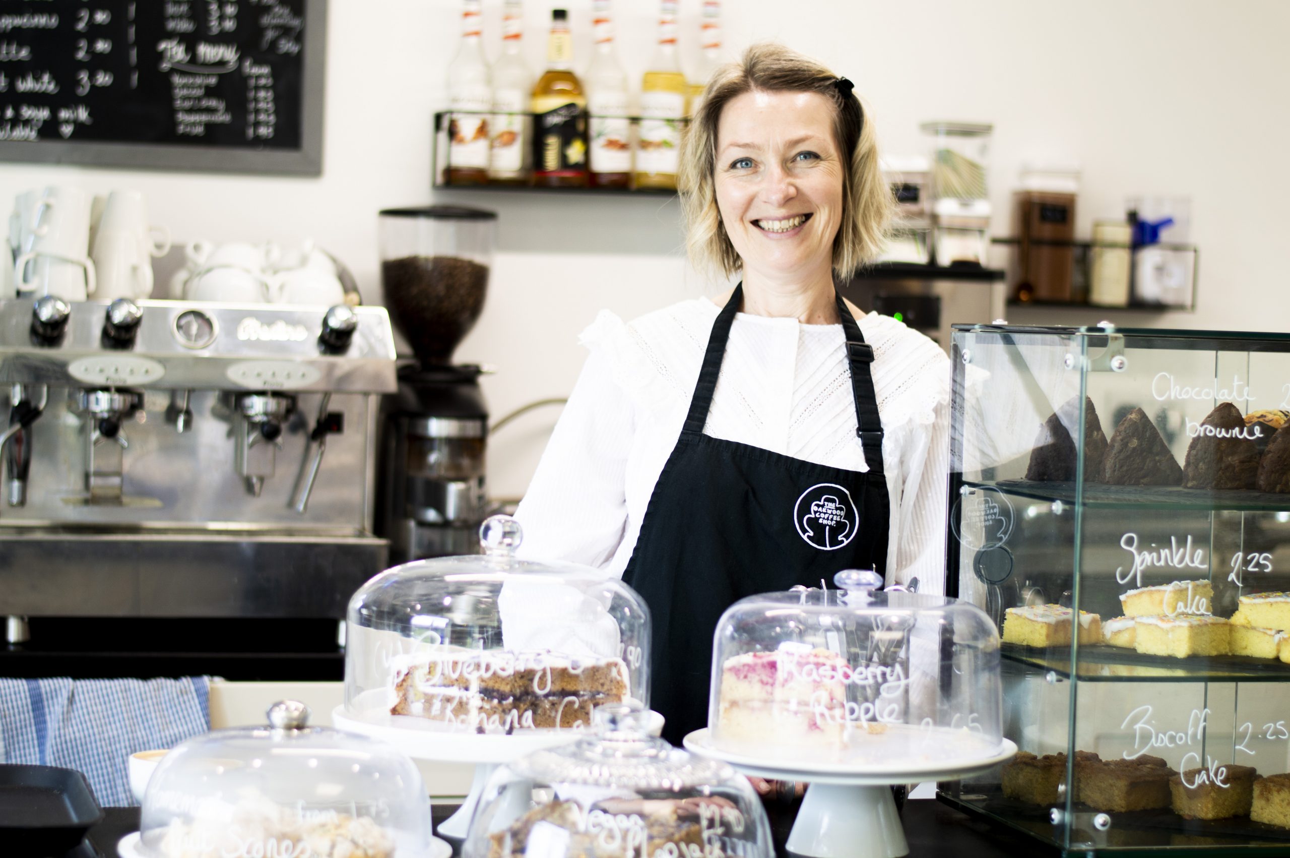 An Oakwood Coffee Shop worker standing at the counter, she is looking at the camera and smiling