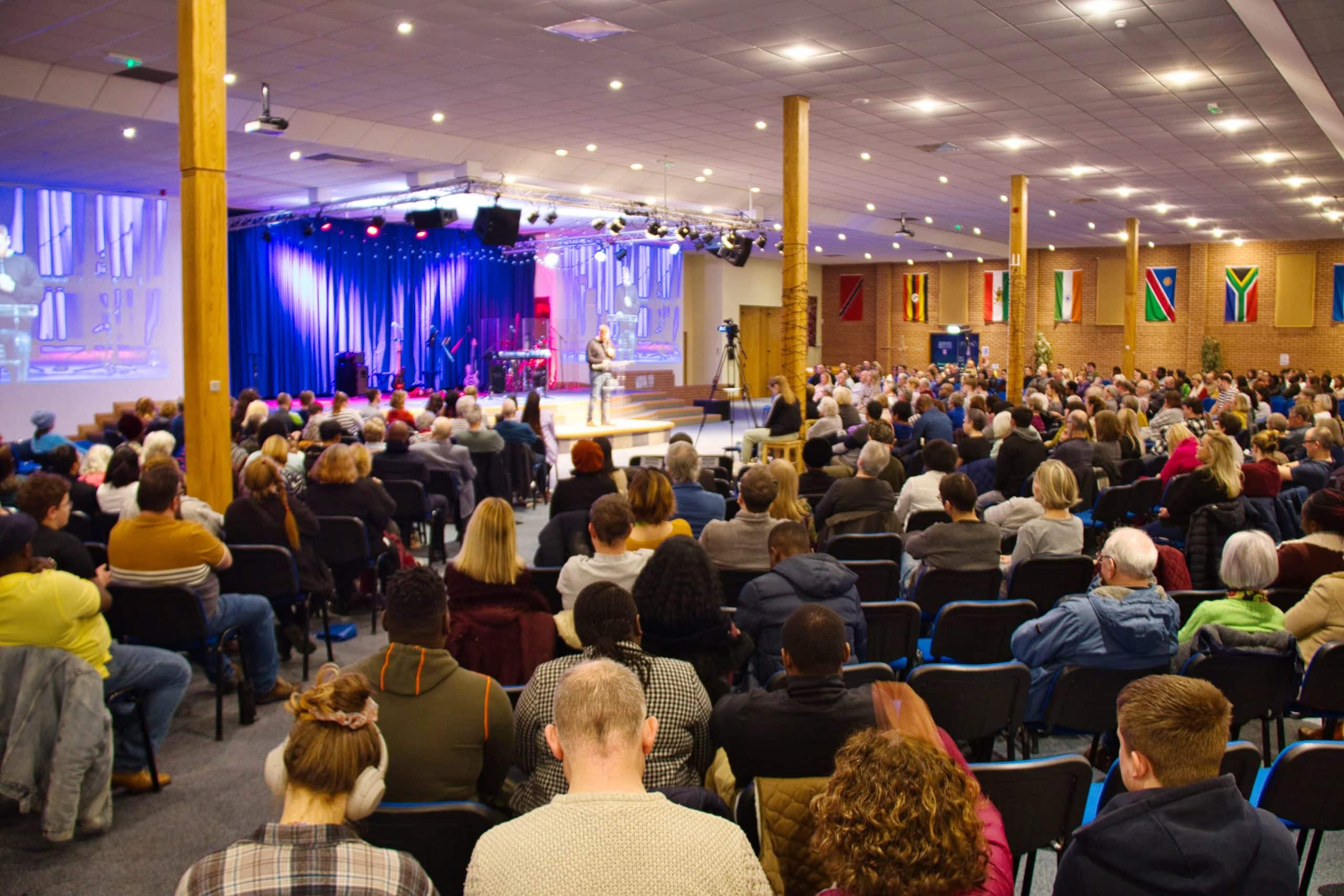 The congregation on a Sunday morning at TVCC, someone is preaching on the stage in the distance