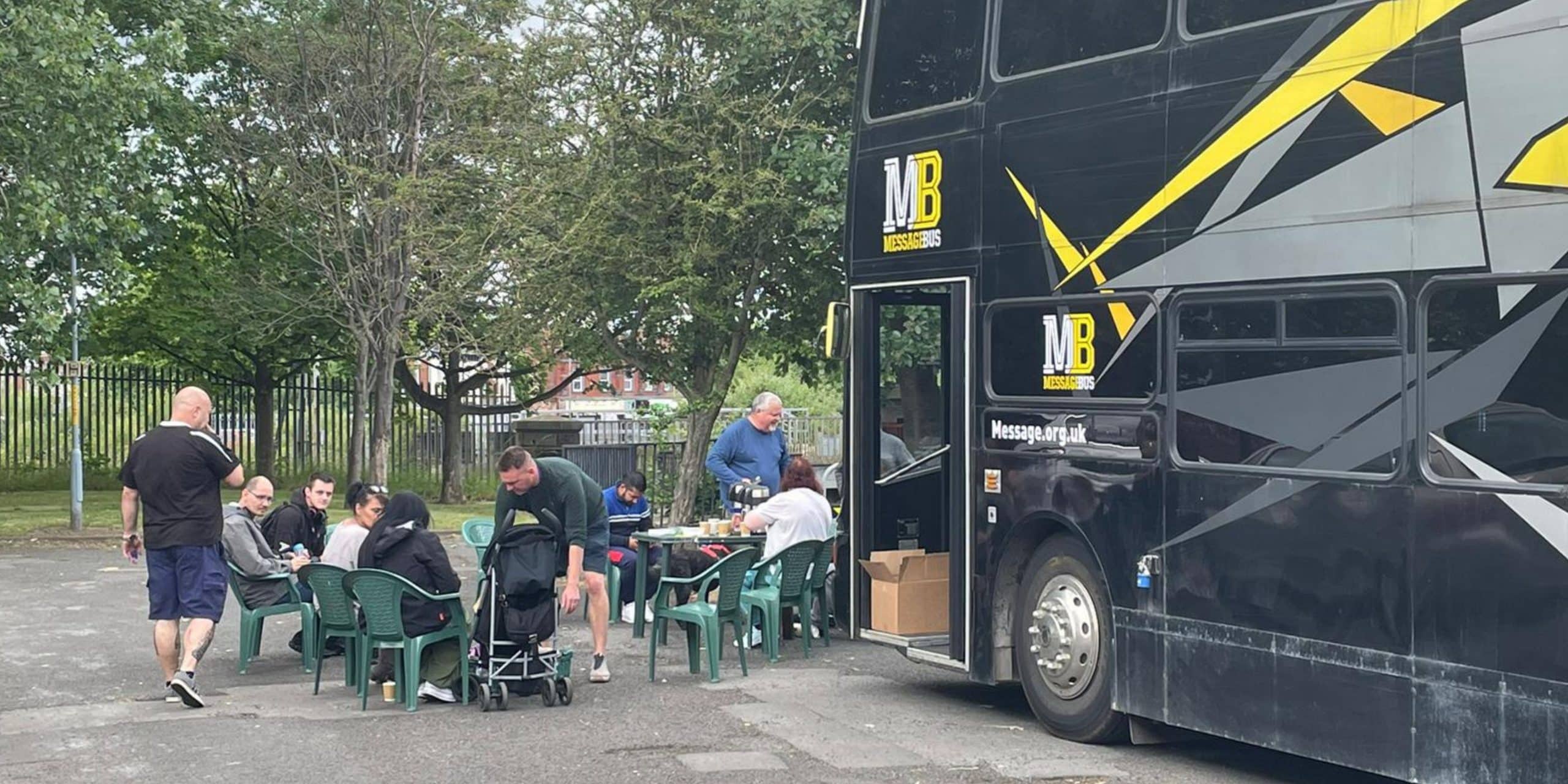 A group of people sat on plastic chairs outside The Message bus